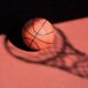 Un pallone di basket e sullo sfondo l'ombra di una retina da canestro