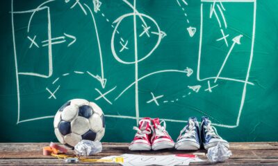 Una lavagna con degli schemi tattici tracciati col gesso e pallone e scarpe da calcio.