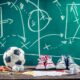 Una lavagna con degli schemi tattici tracciati col gesso e pallone e scarpe da calcio.