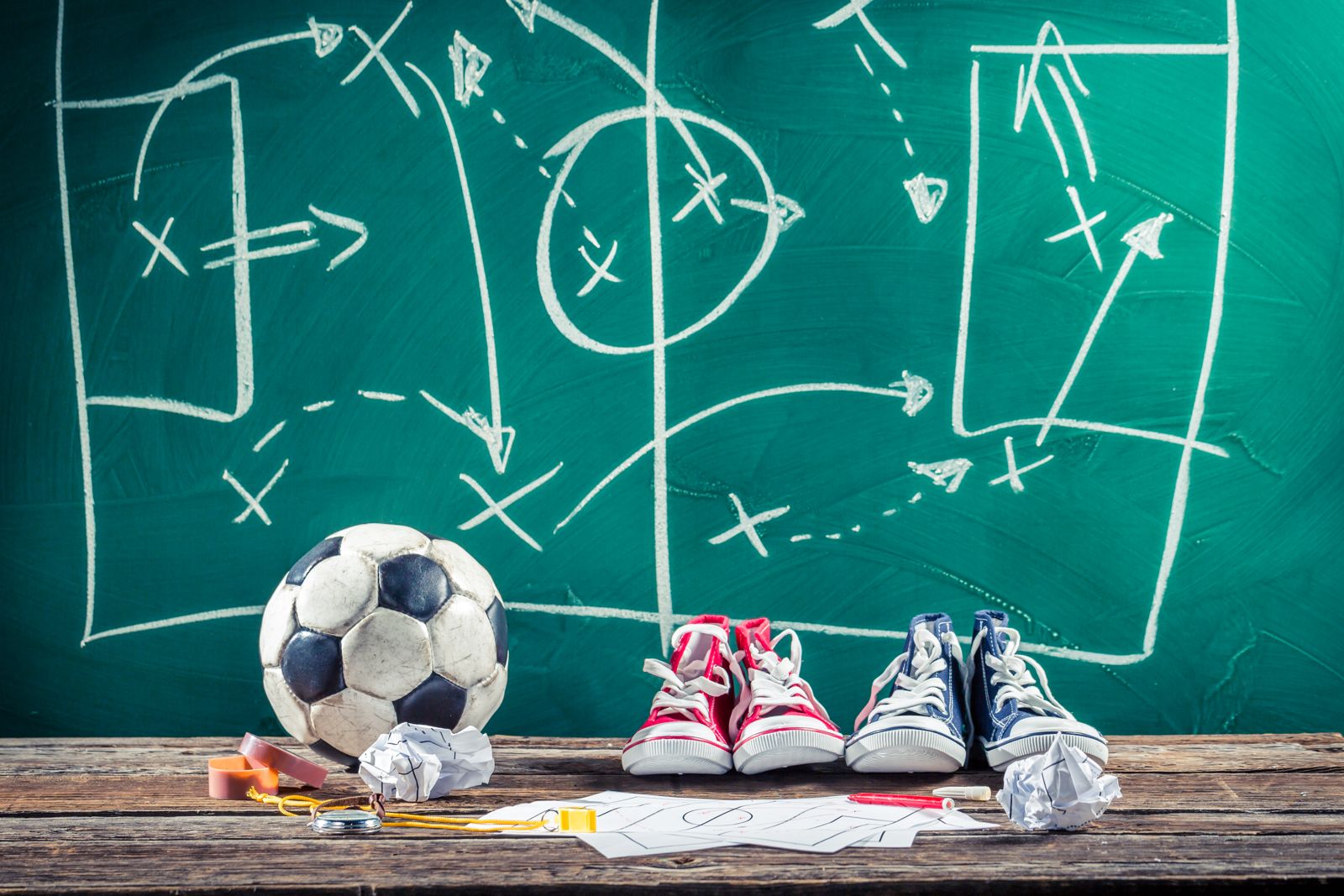 Una lavagna con degli schemi tattici tracciati col gesso e pallone e scarpe da calcio.